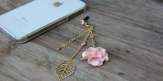 An iphone with a pink flower phone charm attached to it.