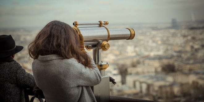 Two women looking through binoculars at the eiffel tower.