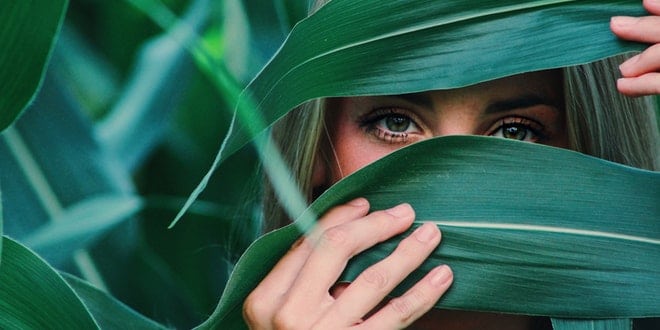A woman is hiding behind a green leaf.