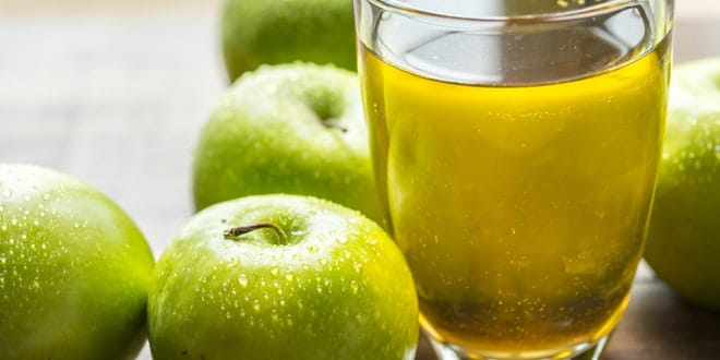 A glass of apple juice next to a bunch of green apples.