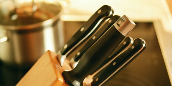 A set of knives in a wooden block on top of a stove.