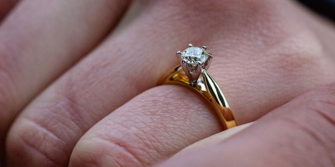 A person's hand holding a diamond engagement ring.