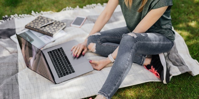 A woman sitting on a blanket with a laptop on her lap.