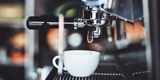 A cup of coffee is being poured into a coffee machine.