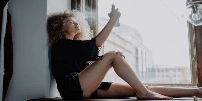 A woman sitting on a window sill with a hairdryer.