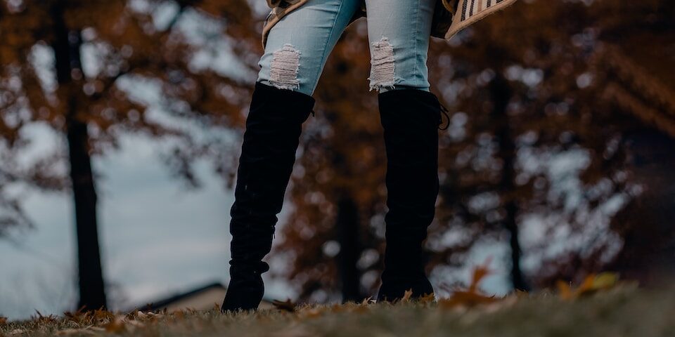 A woman wearing black thigh high boots and jeans.