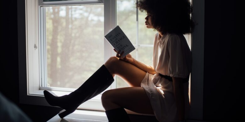 woman in white top black boot holding book