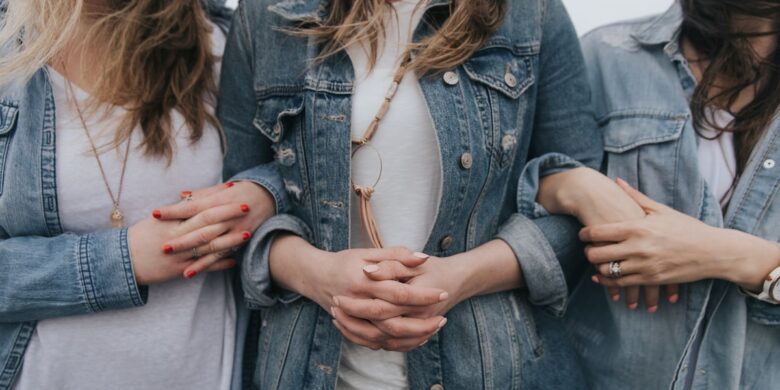 Three women in denim jackets holding hands.