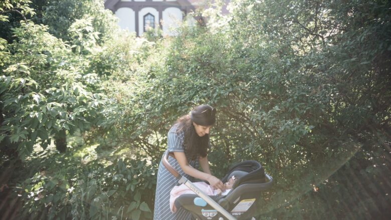 A woman looking at her baby while standing near a stroller.