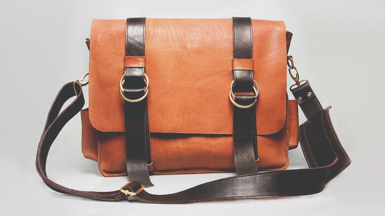 A tan leather messenger bag on a white background.