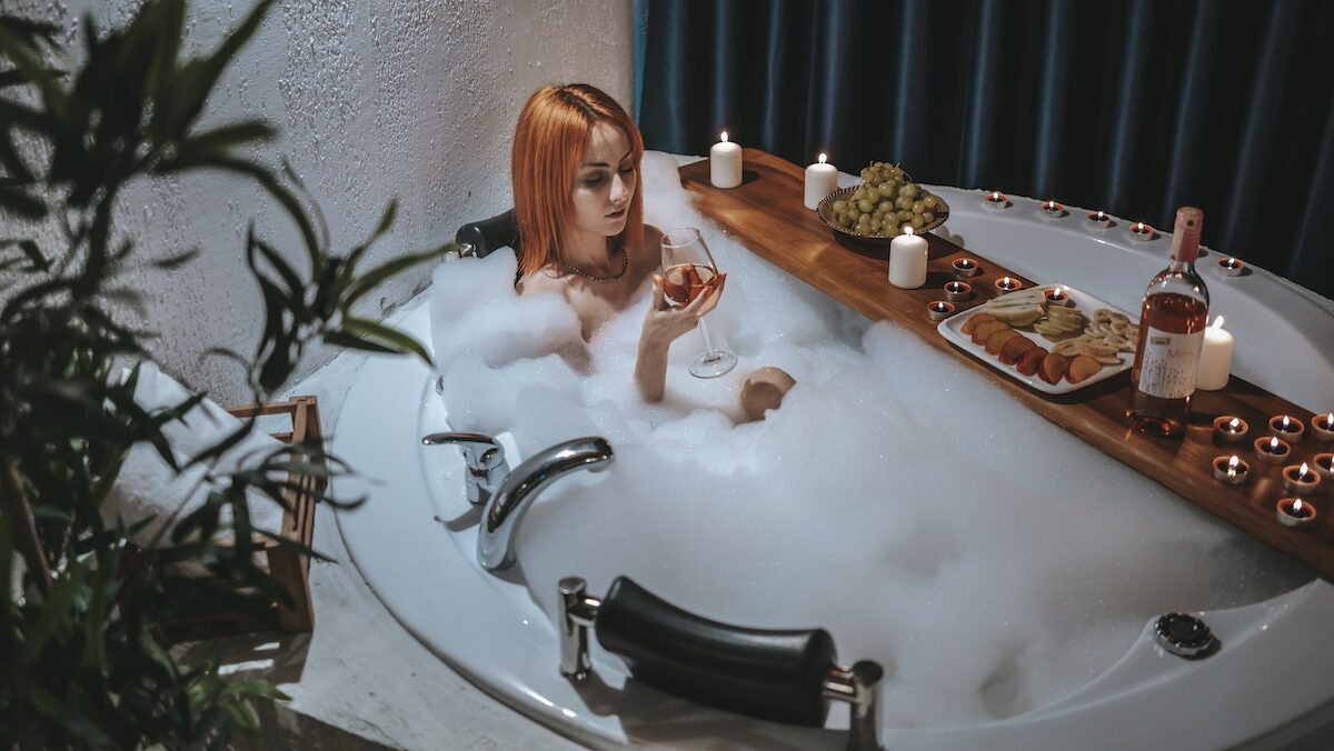 A woman is sitting in a bubble bath with a bottle of wine.