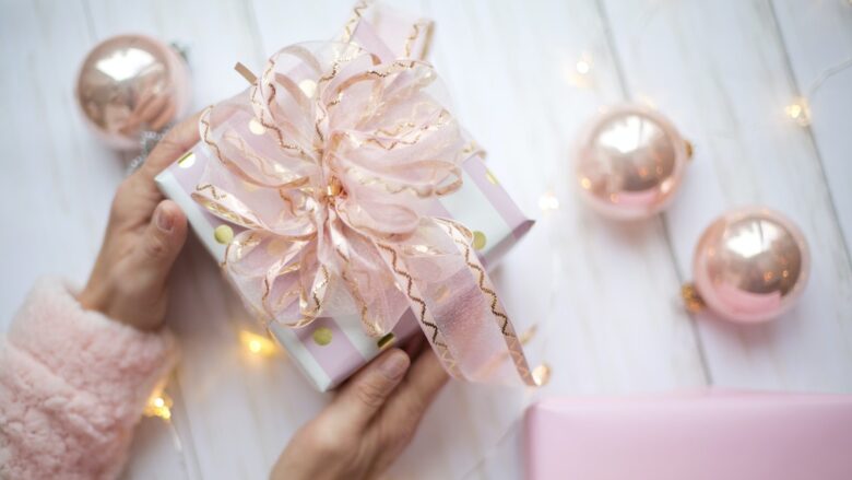 A woman is holding a pink gift box with a pink bow.
