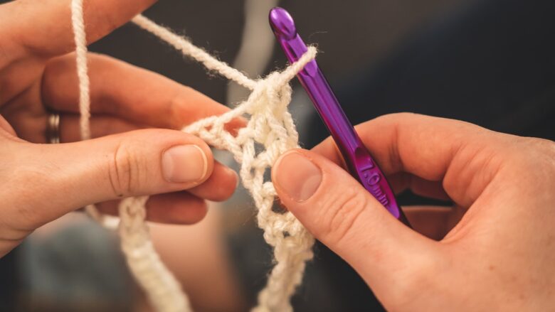 A person crocheting with a purple crochet hook and white yarn.
