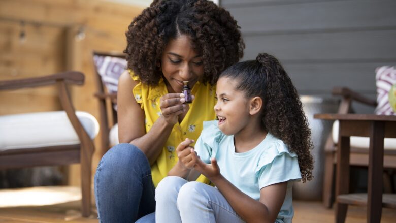 A mother and daughter sitting on a porch smelling a bottle of essential oil perfume.