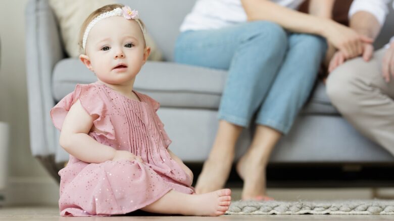A baby girl in pink dress is sitting on the floor with her parents.