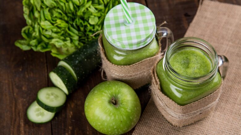 A green smoothie with apples and cucumbers on a wooden table.